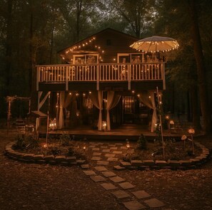 A wooden cabin with a balcony, surrounded by trees and a stone pathway. - Treehouse Retreat with Firepit & Forest Views in Hopkins, South Carolina (Hopkins)