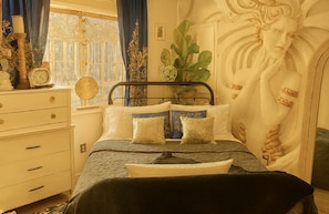 A bedroom with a bed, a dresser, a plant, and a decorative wall.