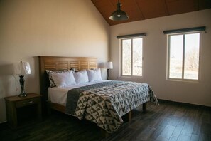 A bedroom with a wooden headboard, a bed with a patterned bedspread, two bedside lamps, and two windows with blinds. - Montelago Cabañas & Resort (San Juan de los Lagos)
