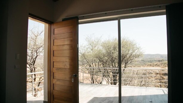 A room with a large sliding glass door leading to an outdoor area with a view of trees and a fence. - Montelago Cabañas & Resort (San Juan de los Lagos)