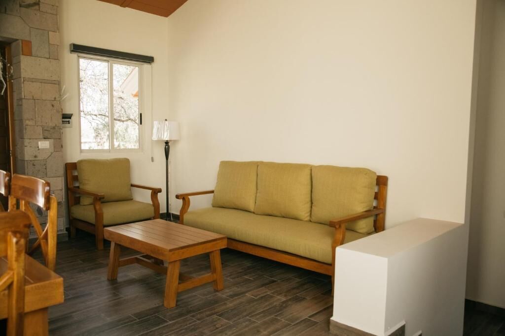 Una sala de estar con un sofá, dos sillones, una mesita de centro de madera y una lámpara.