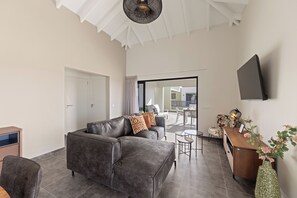 A modern living room with a grey sectional sofa, a coffee table, and a TV mounted on the wall. - Penthouse Casa James Mambo Beach Jacuzzi (Willemstad)