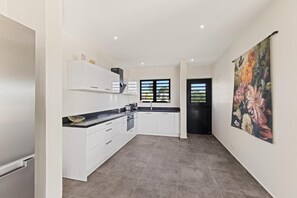 A modern kitchen with white cabinets, a black countertop, and a large floral painting on the wall. - Penthouse Casa James Mambo Beach Jacuzzi (Willemstad)