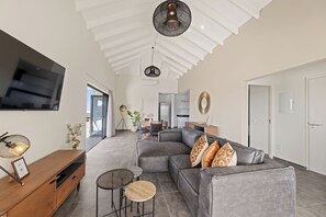 A modern living room with a grey sectional sofa, a wooden console table, a round coffee table, and a TV mounted on the wall. - Penthouse Casa James Mambo Beach Jacuzzi (Willemstad)