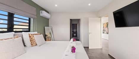 A hotel room with a bed, a flat-screen TV mounted on the wall, and a window with blinds.