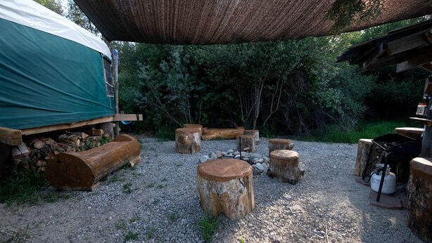 A rustic outdoor area with a covered seating area, wooden logs, and a gas stove. - Glamping Yurt with Firepit, Hammock & Wood Stove in Garden Valley, Idaho (Garden Valley)
