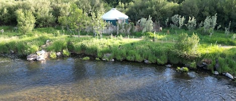 Une rivière aux eaux claires, bordée d’une végétation luxuriante et surmontée d’une petite construction dotée d’un toit conique.