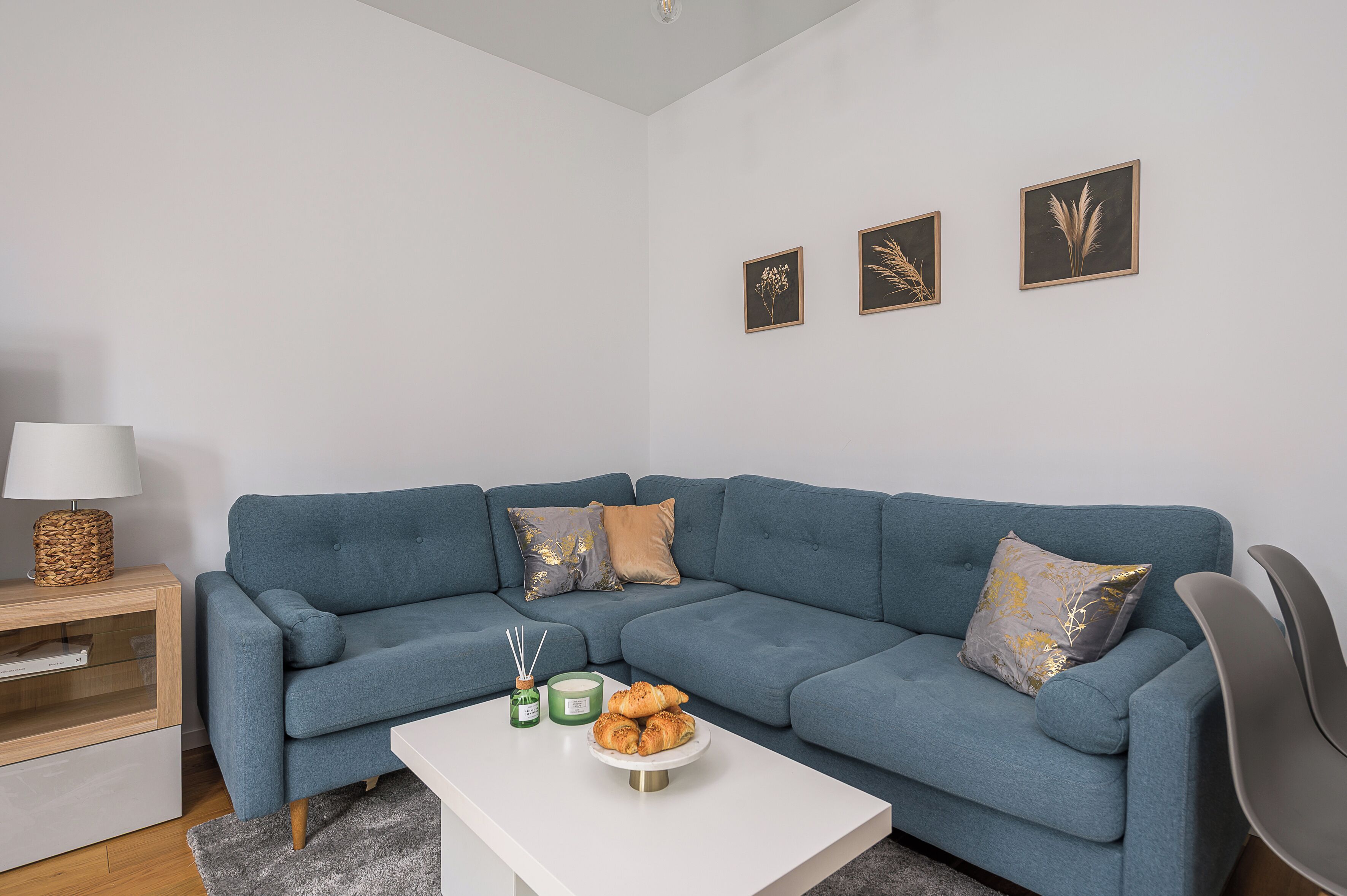 A living room with a blue sofa, a white coffee table with candles and pastries, and a lamp on a side table.