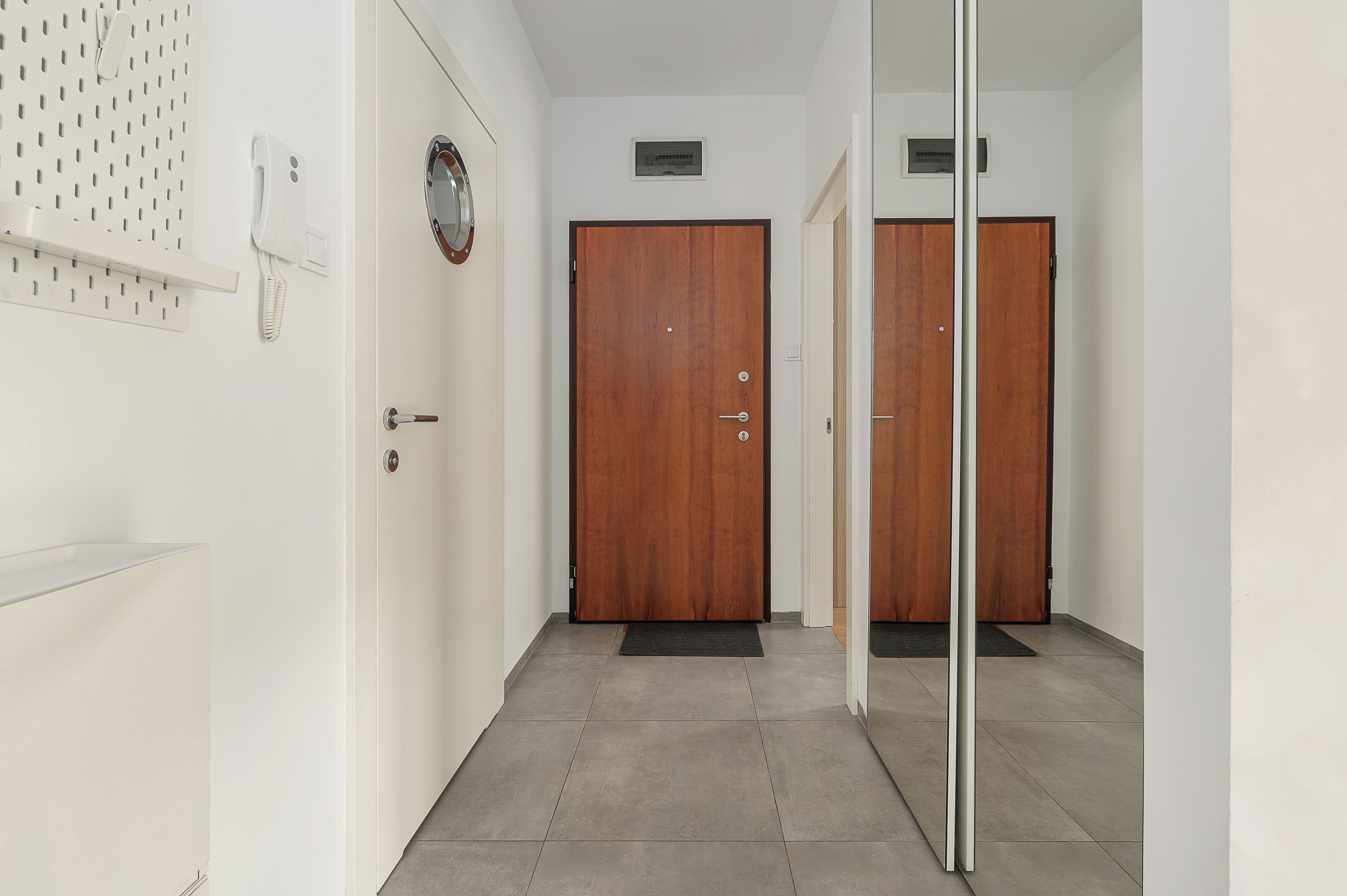 A hallway with a wooden door, a white wall, and a tiled floor.