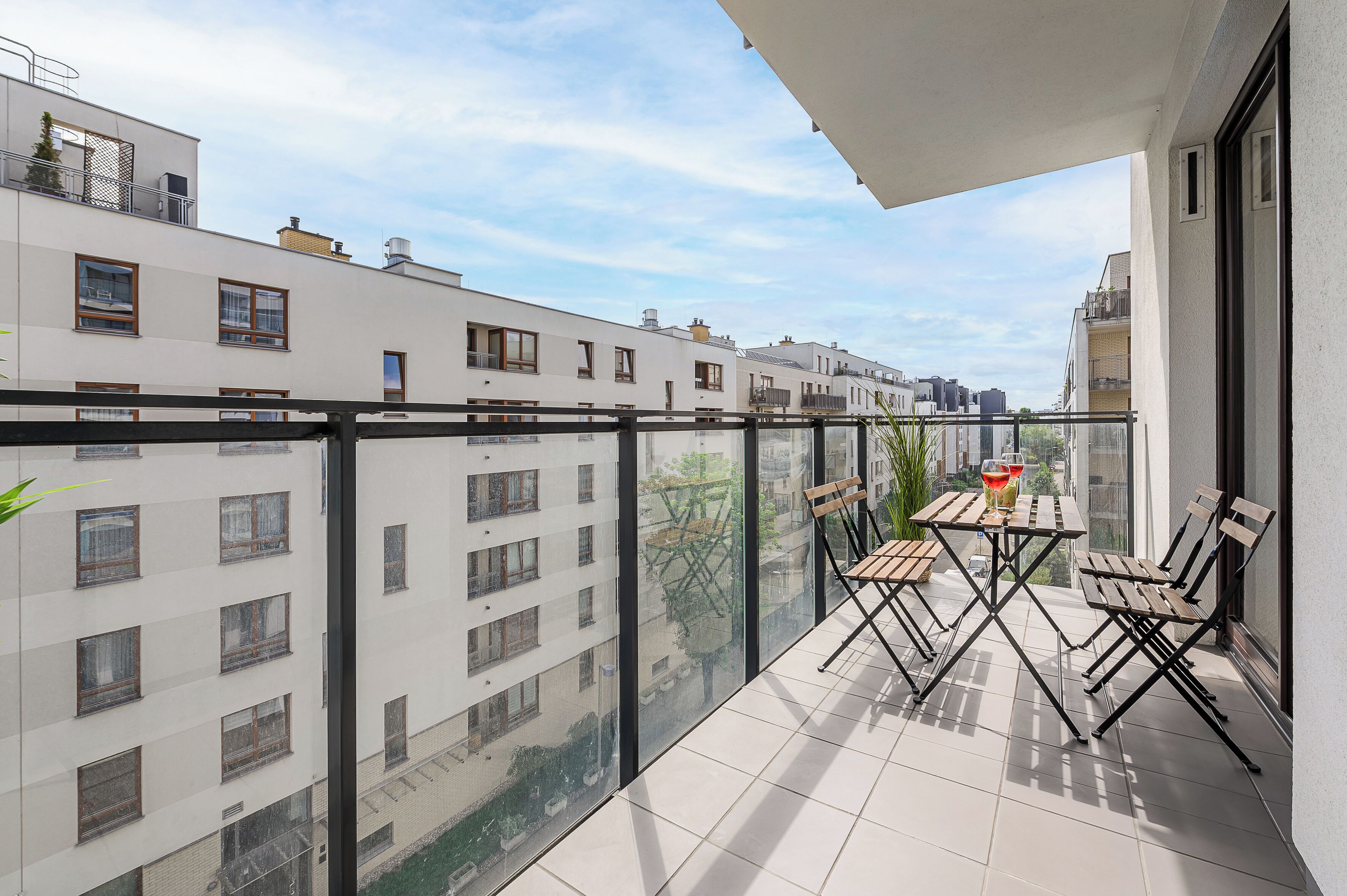 A balcony with a table and chairs, overlooking a cityscape with multiple buildings.