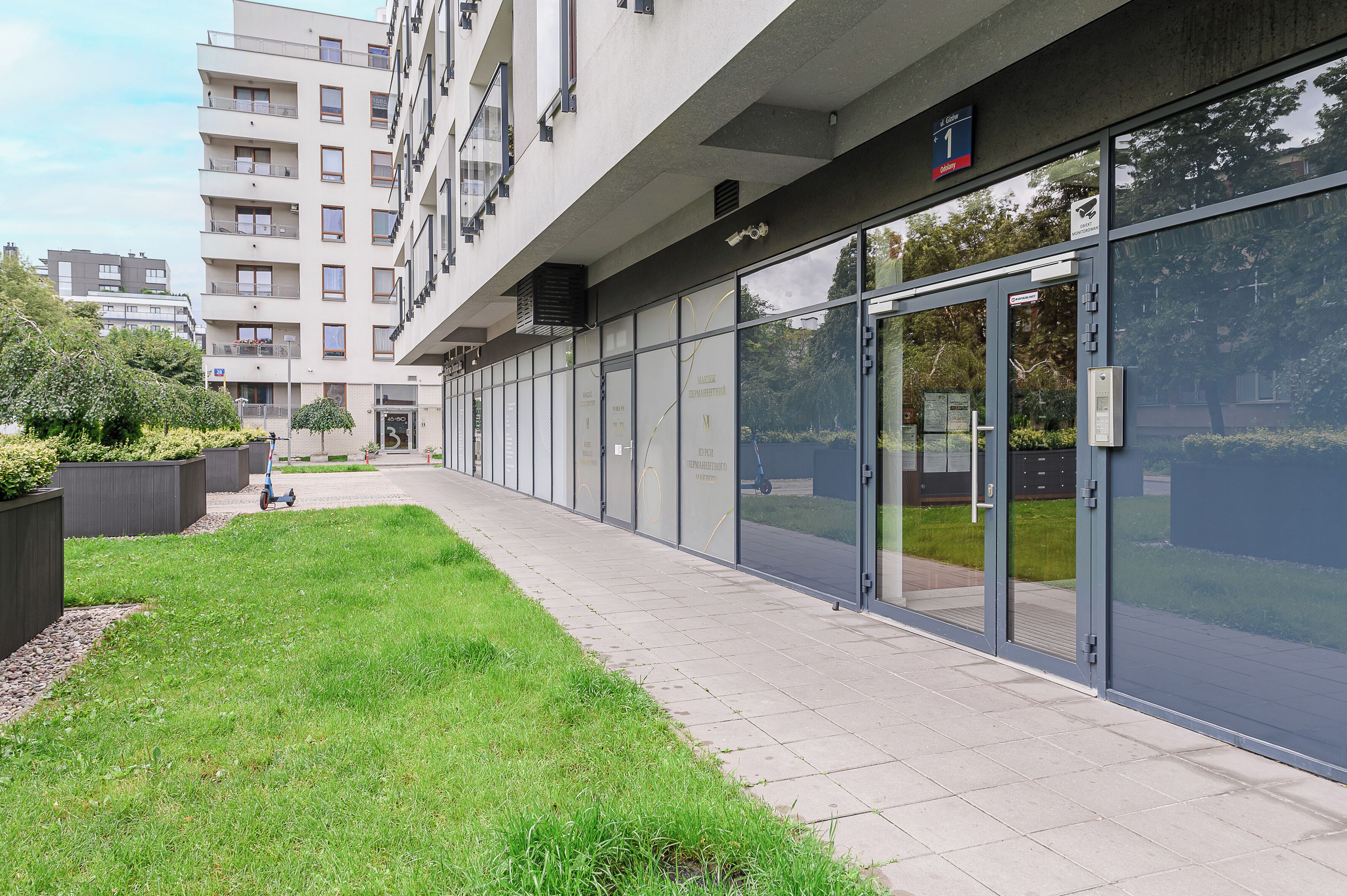 A modern building with a glass facade, a paved walkway, and a small grassy area.