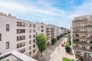 Un edificio residencial de varios pisos con balcones, una calle peatonal y un árbol en primer plano.