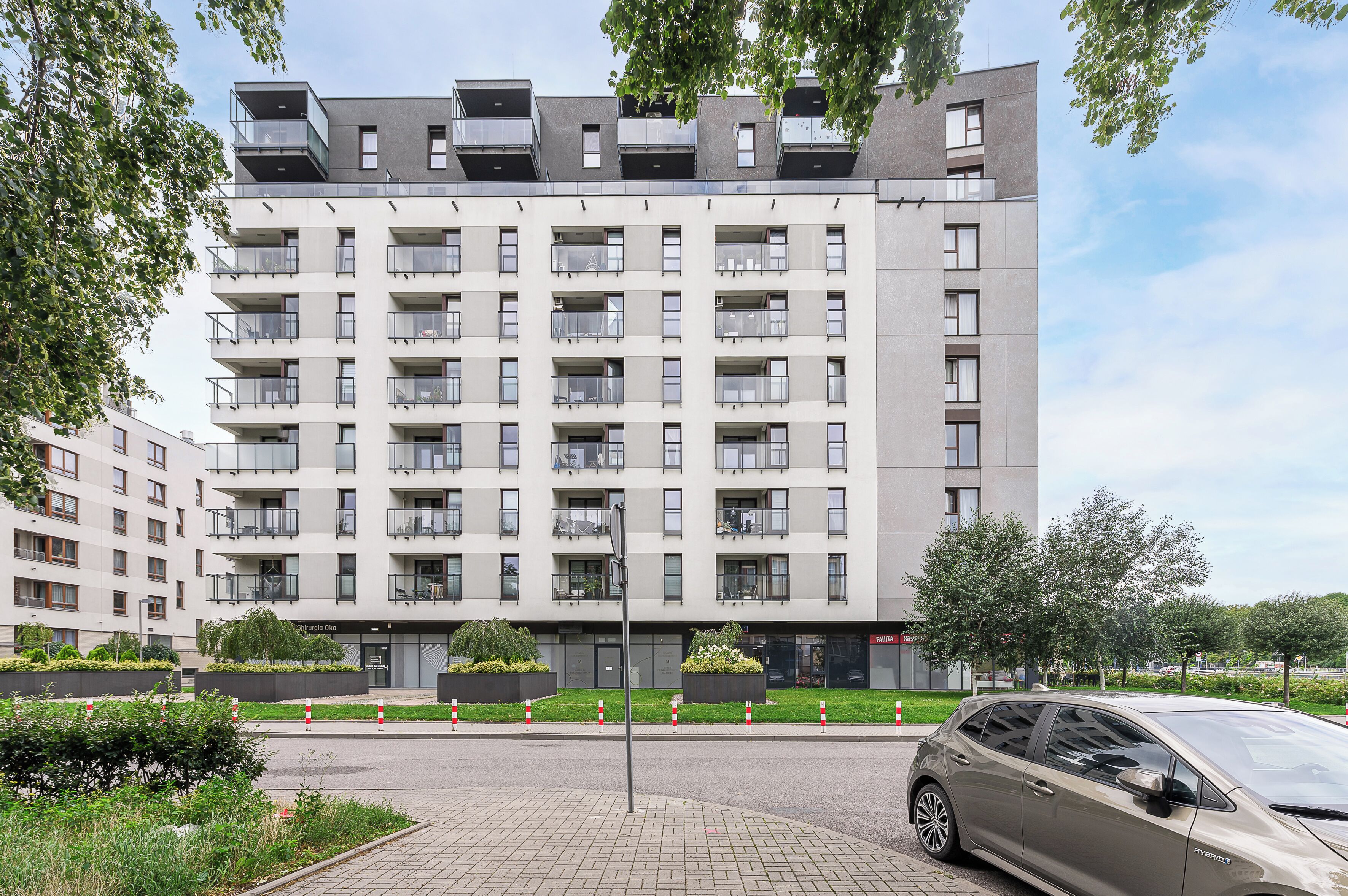 A modern multi-story residential building with balconies, a parking area, and a car.