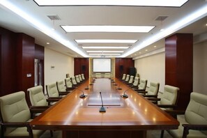 Een vergaderzaal met een lange tafel, stoelen, een projectiescherm en een presentatiescherm.