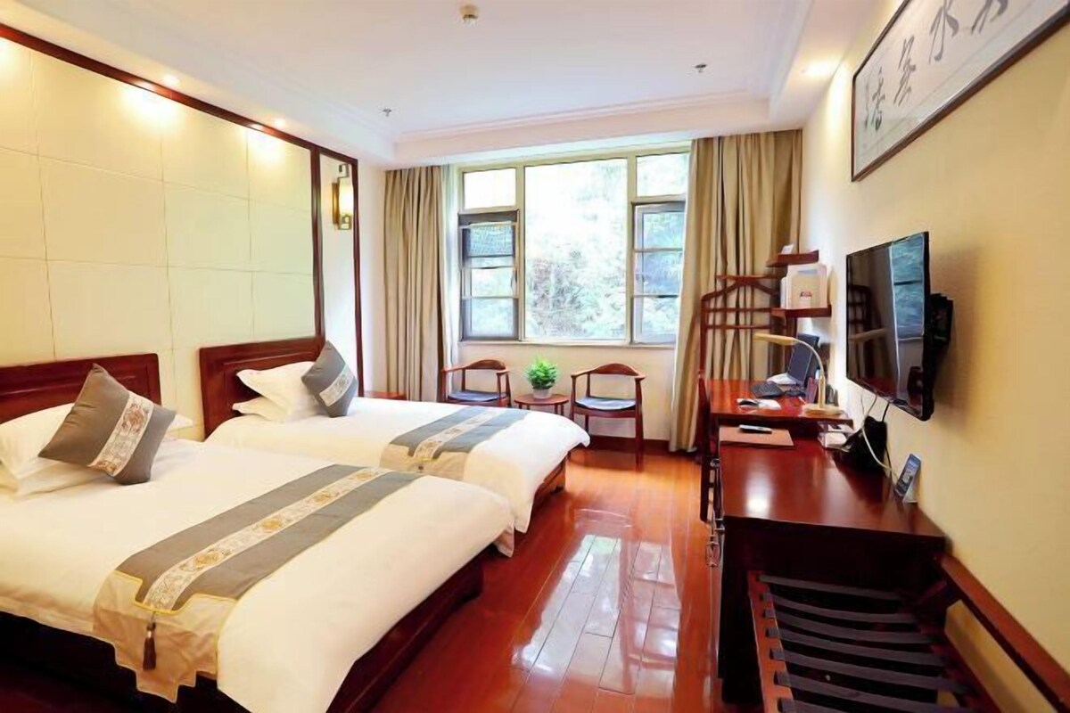 A hotel room with two beds, a desk, a chair, a television, and a window with curtains.