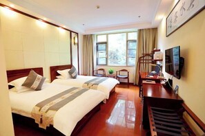 Une chambre d’hôtel avec deux lits, un bureau, une chaise, une télévision et une fenêtre avec des rideaux.