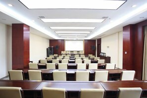 Un salón de conferencias con filas de mesas y sillas, una pantalla de proyector y una zona para presentaciones.