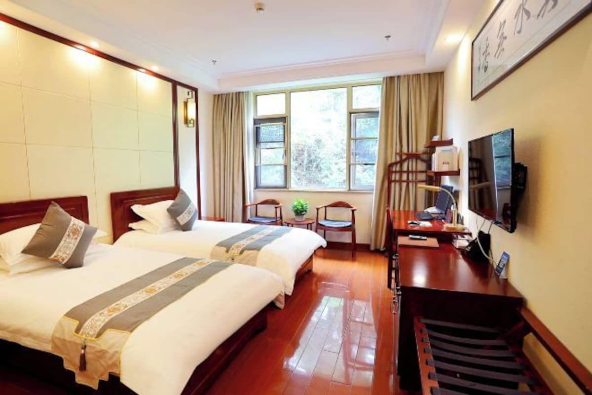 A hotel room with two beds, a desk, a chair, a television, and a window with curtains.