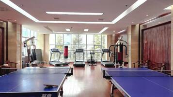 Ein Raum mit Tischtennisplatten, Fitnessgeräten und großen Fenstern.