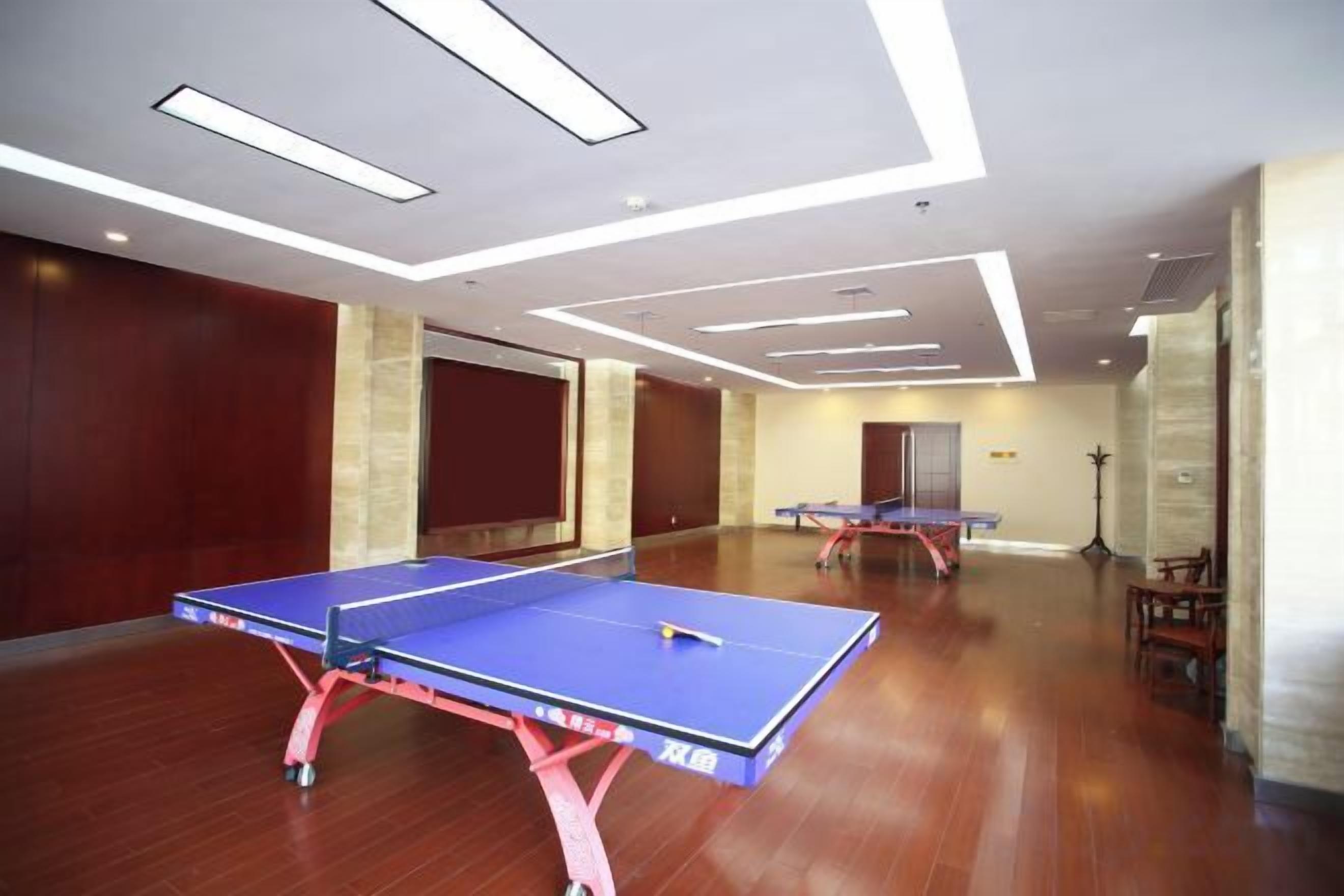 A room with two ping pong tables, wooden flooring, and a modern ceiling design.