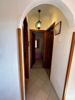 A hallway with an arched ceiling, wooden doors, a tiled floor, and a hanging light fixture. - Beach Walk Apartments - San Teodoro (San Teodoro)