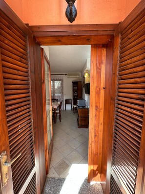 A wooden-framed doorway leading to a room with a tiled floor, a dining table, and a television. - Beach Walk Apartments - San Teodoro (San Teodoro)