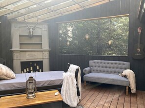 A cozy room with a fireplace, a sofa, a bench, and a large window overlooking greenery.