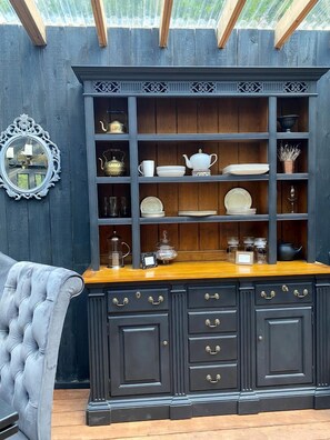 A dark wooden cabinet with multiple shelves and drawers, a mirror, and a cushioned chair.
