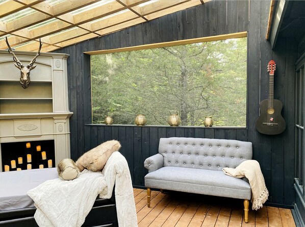 Ein gemütliches Zimmer mit einem grauen Sofa, einem weißen Fellüberwurf und einer Gitarre an der Wand.