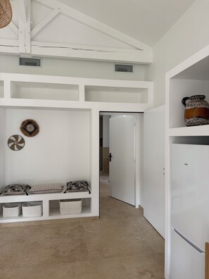 Ein Flur mit weißen Wänden, einem Deckenventilator, einer Tür zu einem anderen Raum und einem weißen Kühlschrank.