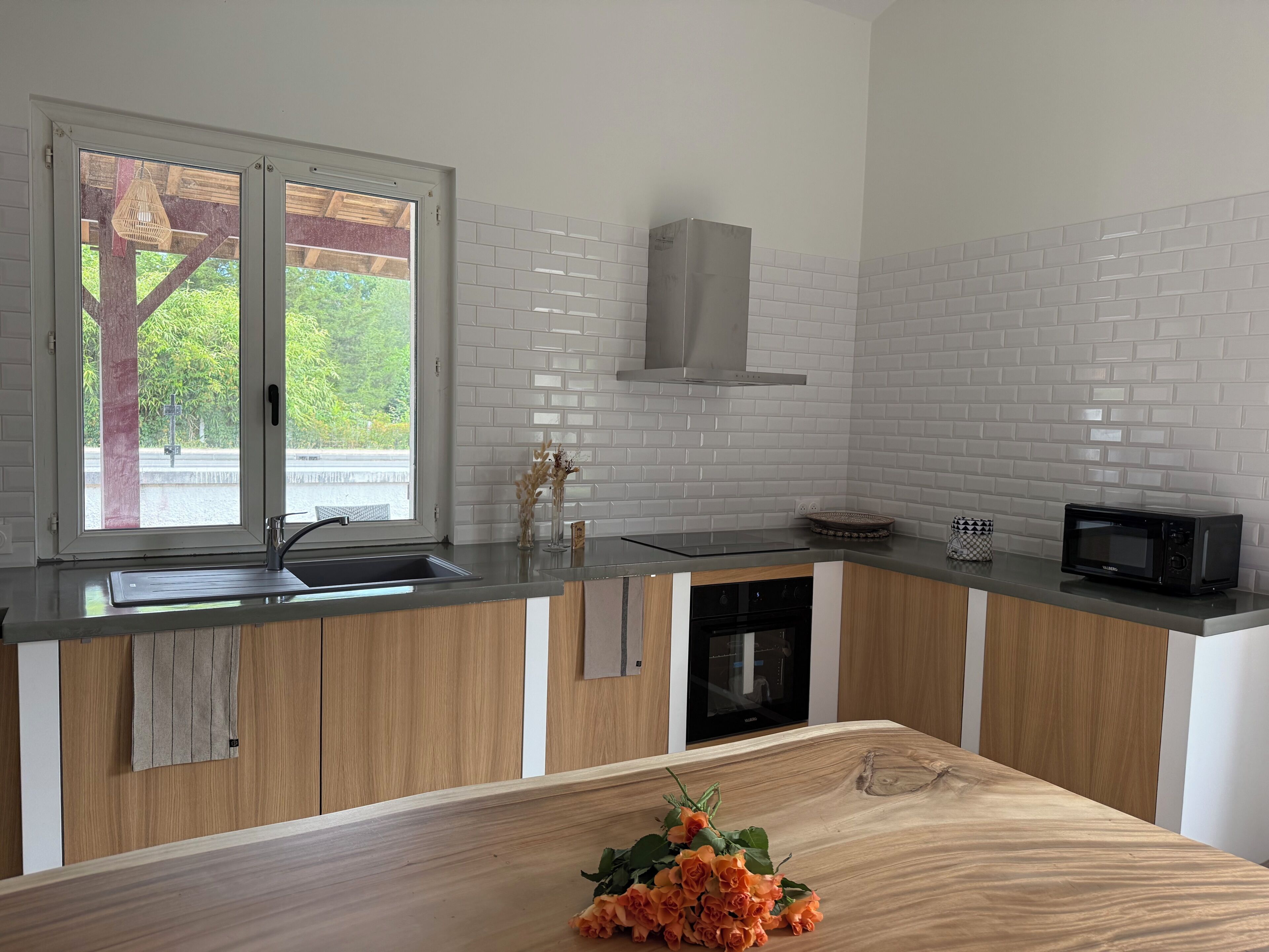 A modern kitchen with a wooden countertop, a built-in microwave, and a window with a view of greenery.