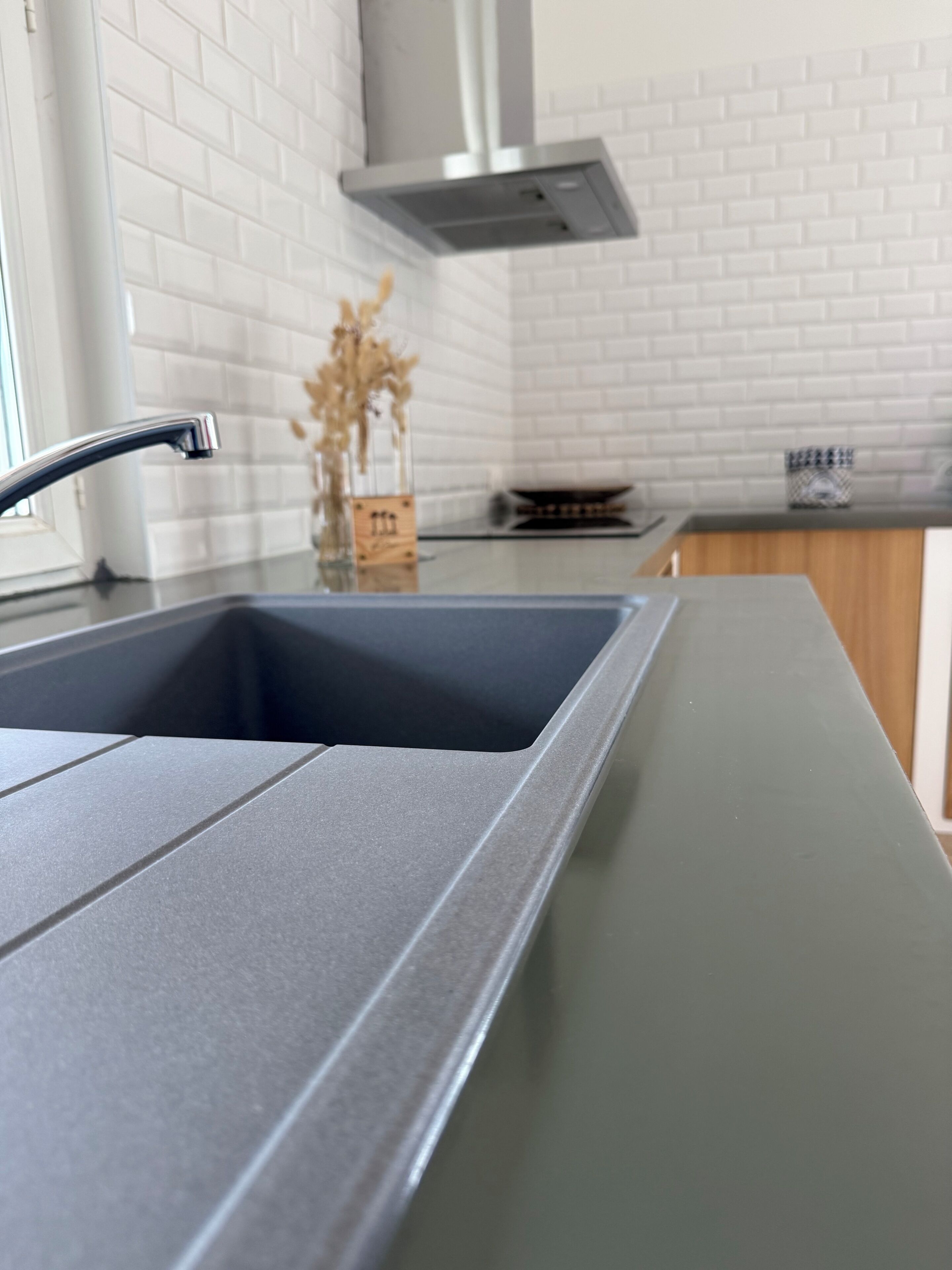 Una cocina con un lavamanos moderno, salpicadero de azulejos blancos y una campana extractora de acero inoxidable.