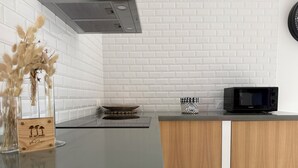 A modern kitchen with white brick backsplash, a wooden countertop, a black microwave, and a decorative bowl. - SOLEO Vacation Home (Solférino)