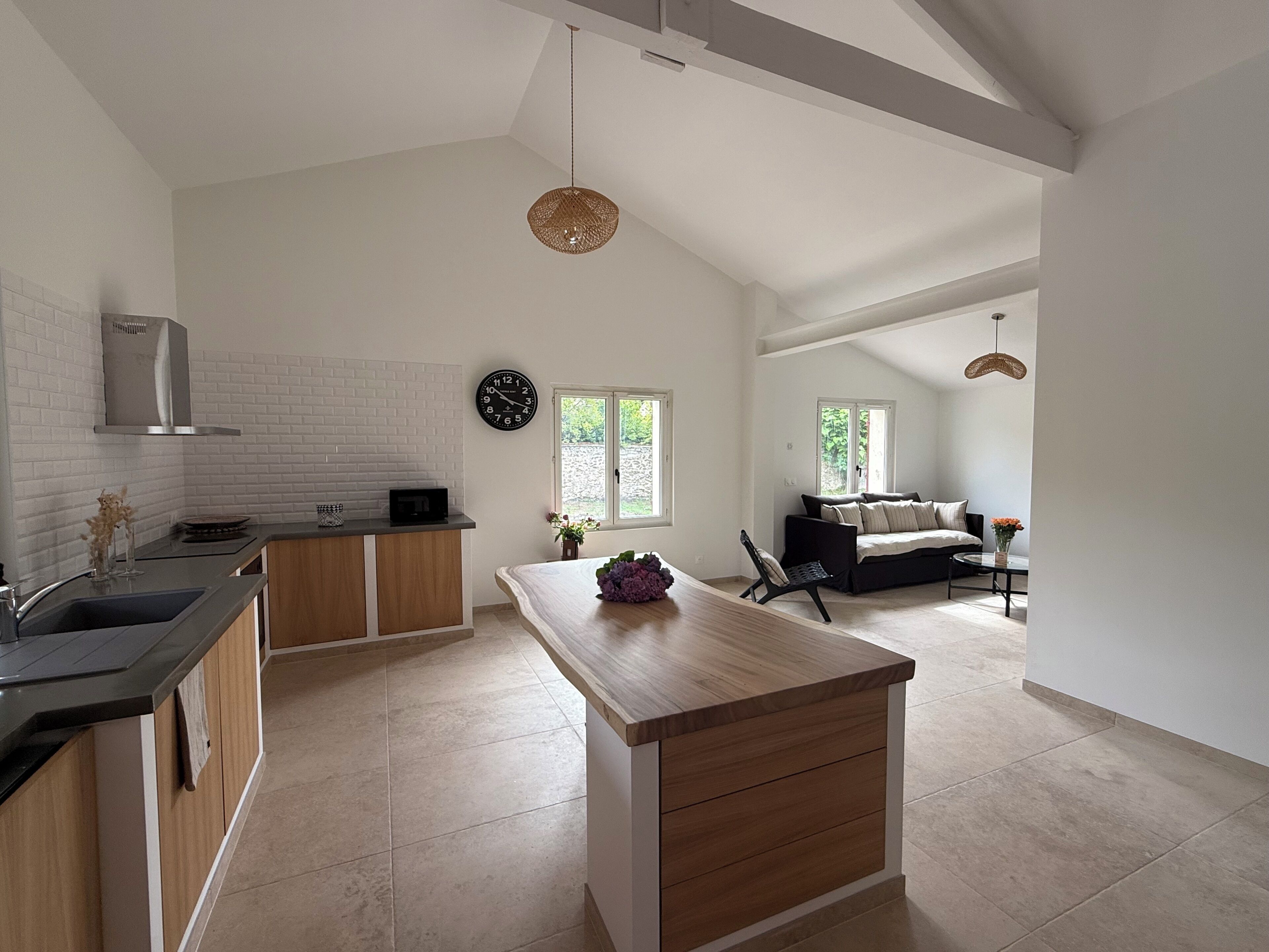 A spacious kitchen with a central island, a dining area with a sofa, and a view of greenery outside.
