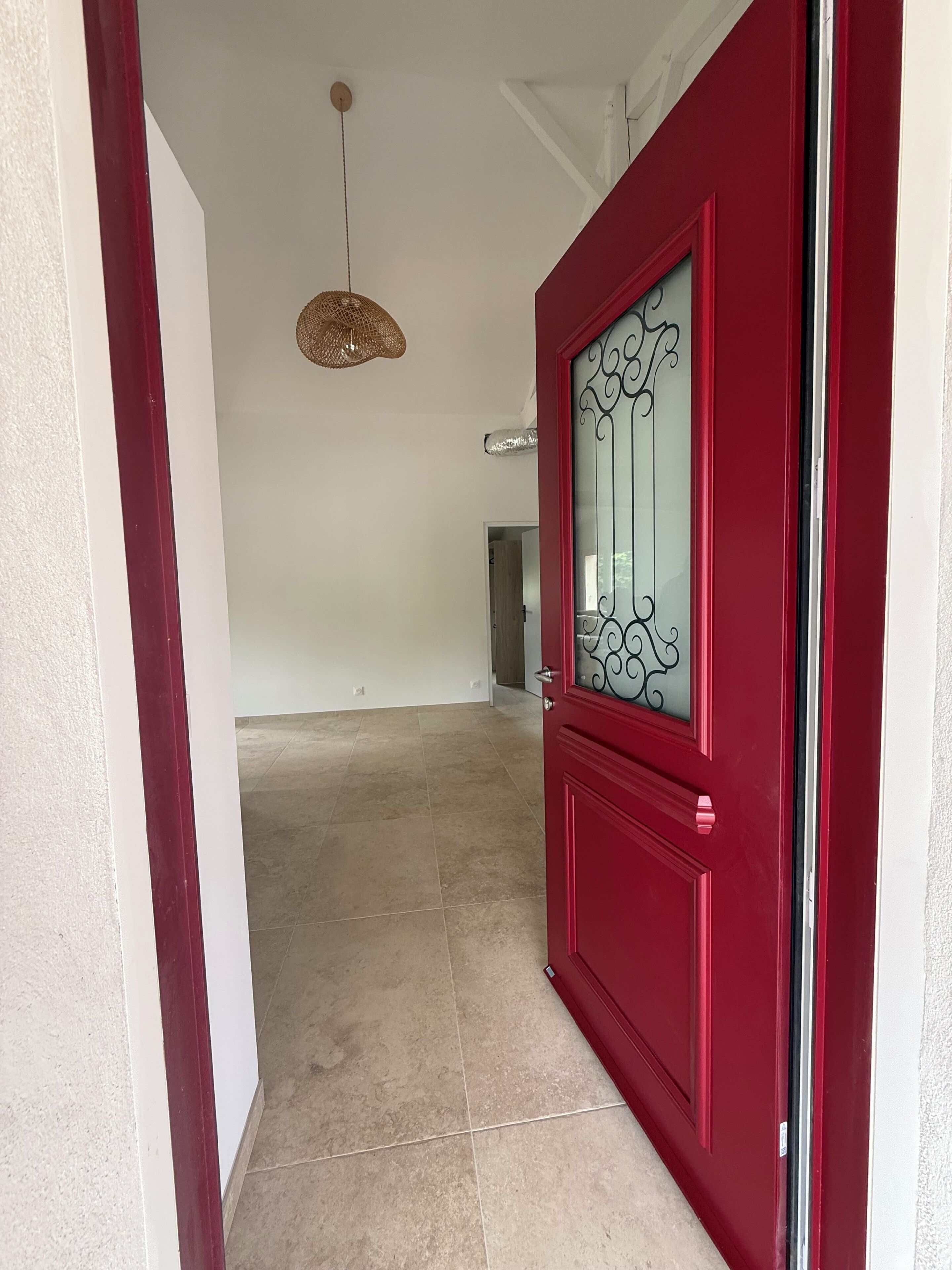 Un couloir avec une porte rouge, un luminaire suspendu et un sol carrelé.