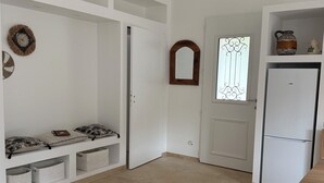 A spacious room with a white wardrobe, a bench with cushions, a small window with decorative glass, and a white refrigerator. - SOLEO Vacation Home (Solférino)