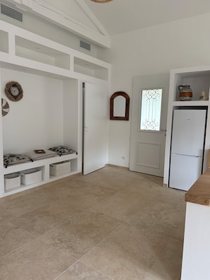 Ein geräumiges Zimmer mit einem weißen Kleiderschrank, einer Sitzbank mit Kissen, einem kleinen Fenster mit Verzierglas und einem weißen Kühlschrank.