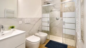Ein modernes Badezimmer mit einer gläsernen Duschkabine, einem weißen Waschbecken und einem Bidet.