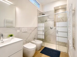 A modern bathroom with a glass-enclosed shower, a white sink, and a bidet.