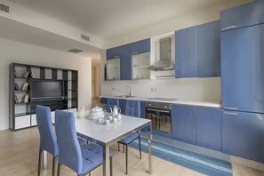A modern kitchen with blue cabinets, a dining table with chairs, and a built-in TV.