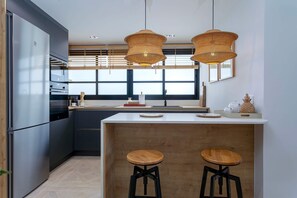 Een moderne keuken met roestvrijstalen apparatuur, een centraal kookeiland met krukken, en grote ramen.