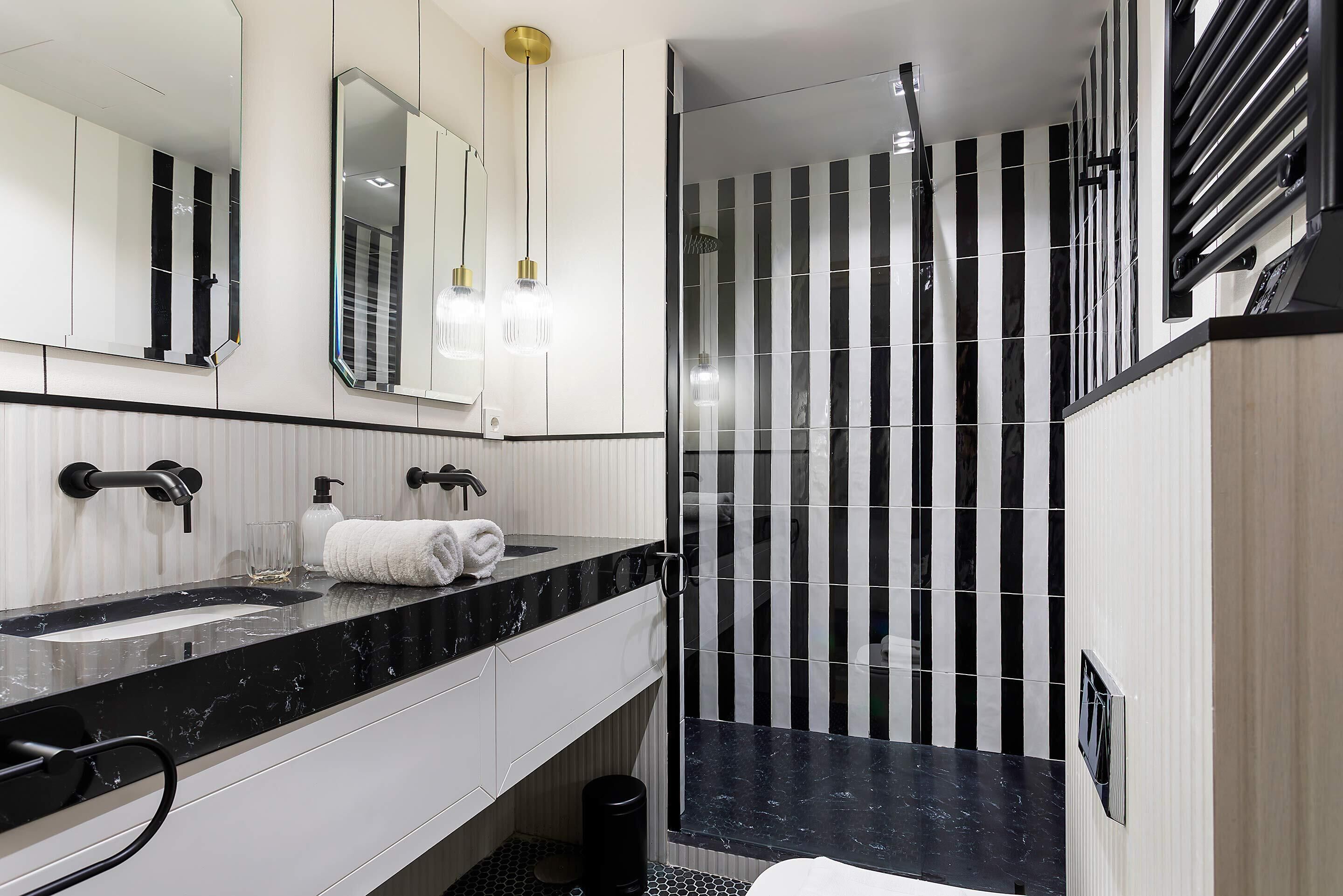 Une salle de bain moderne avec une douche à rayures noires et blanches, un grand miroir et un comptoir en marbre noir.