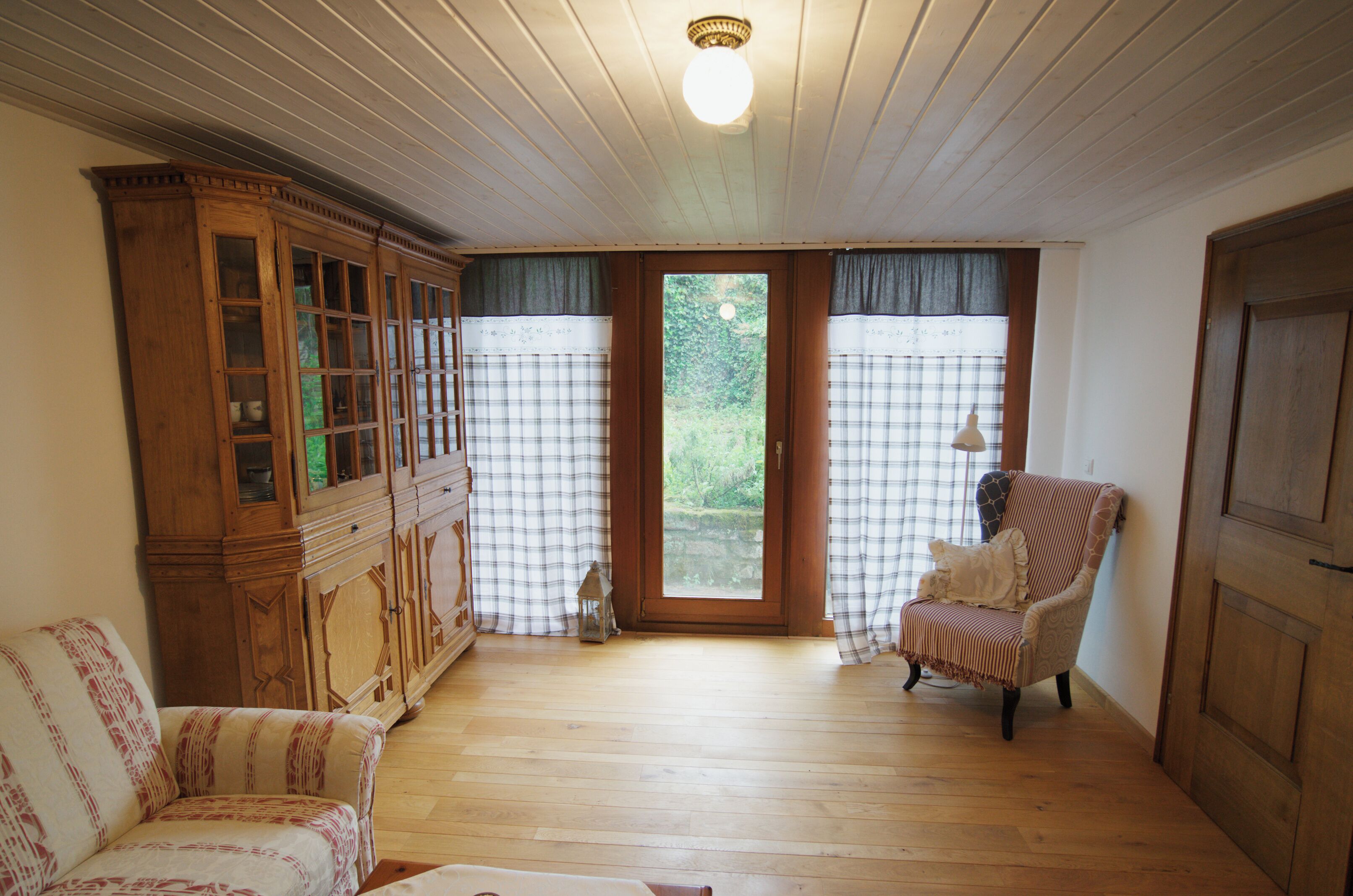 A room with wooden flooring, a cabinet with glass doors, a chair, and a door.