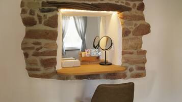 A stone-framed mirror with a light above it, a chair, and a window with curtains.