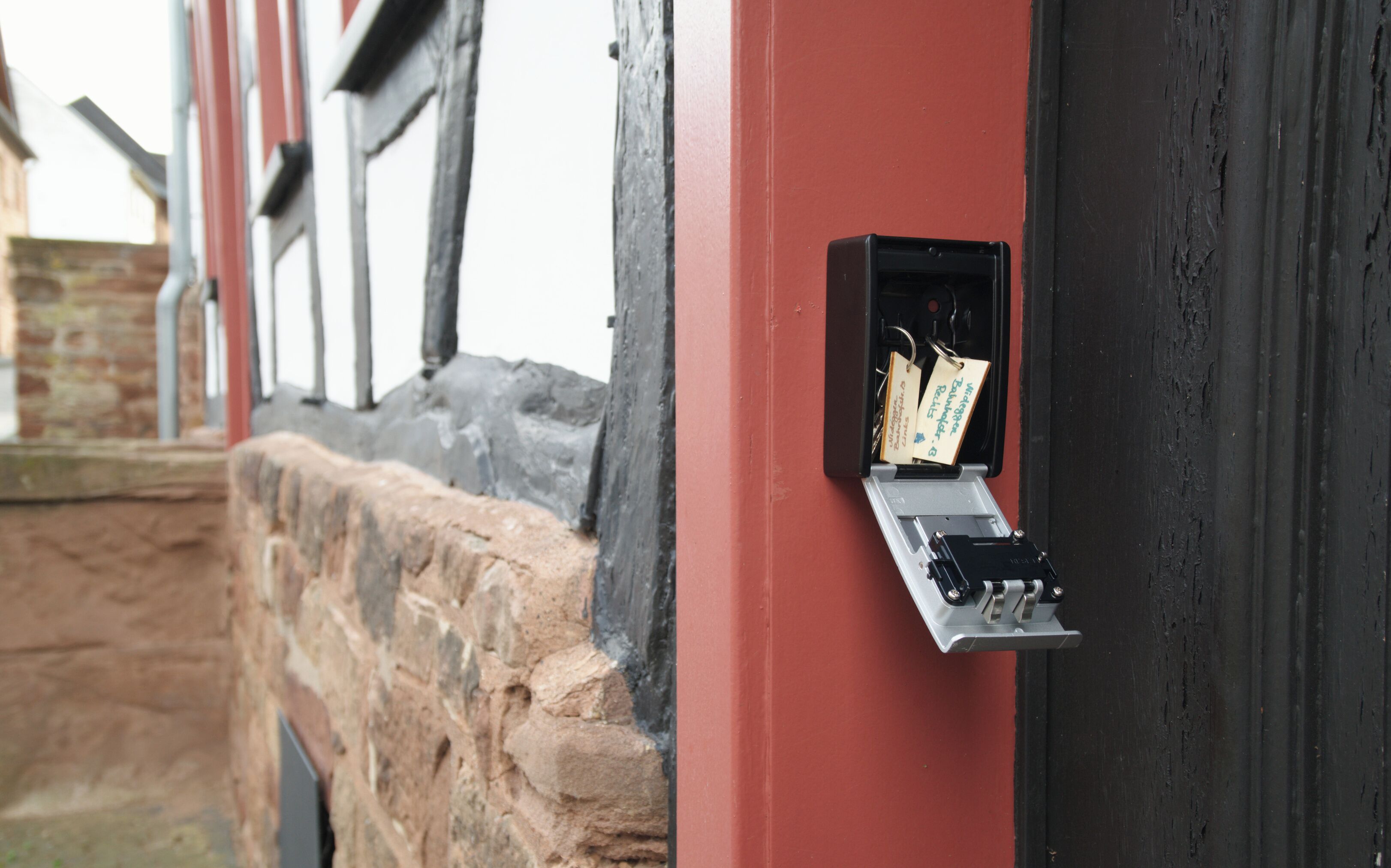 Een elektriciteitskast met sleutels en labels, bevestigd aan een rode muur naast een stenen muur.