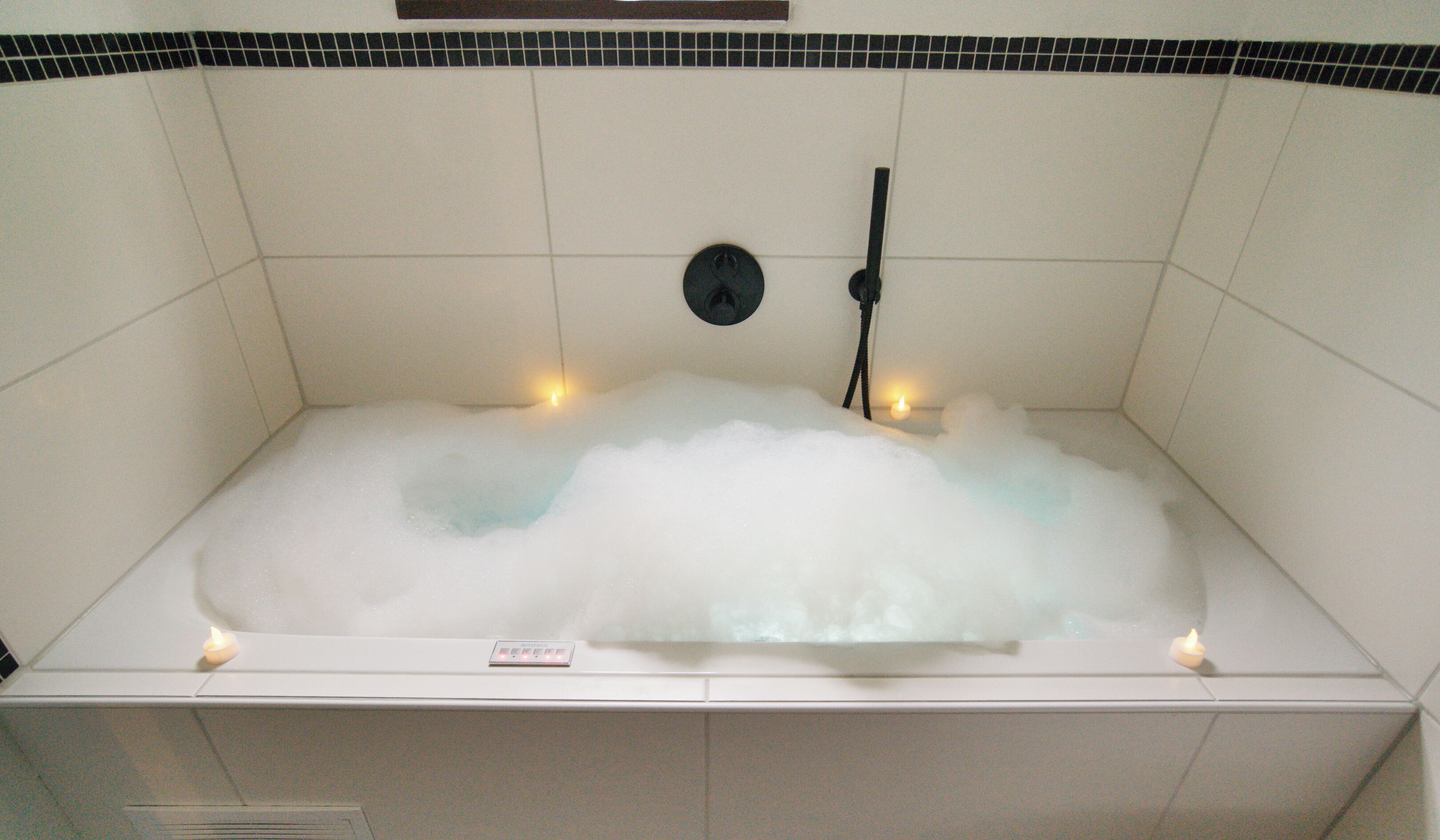 Eine Wanne voller Blasen, ein schwarzer Wasserhahn und zwei Kerzen.