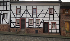A traditional half-timbered building with a black door, red-framed windows, and a stone staircase leading to the entrance.
