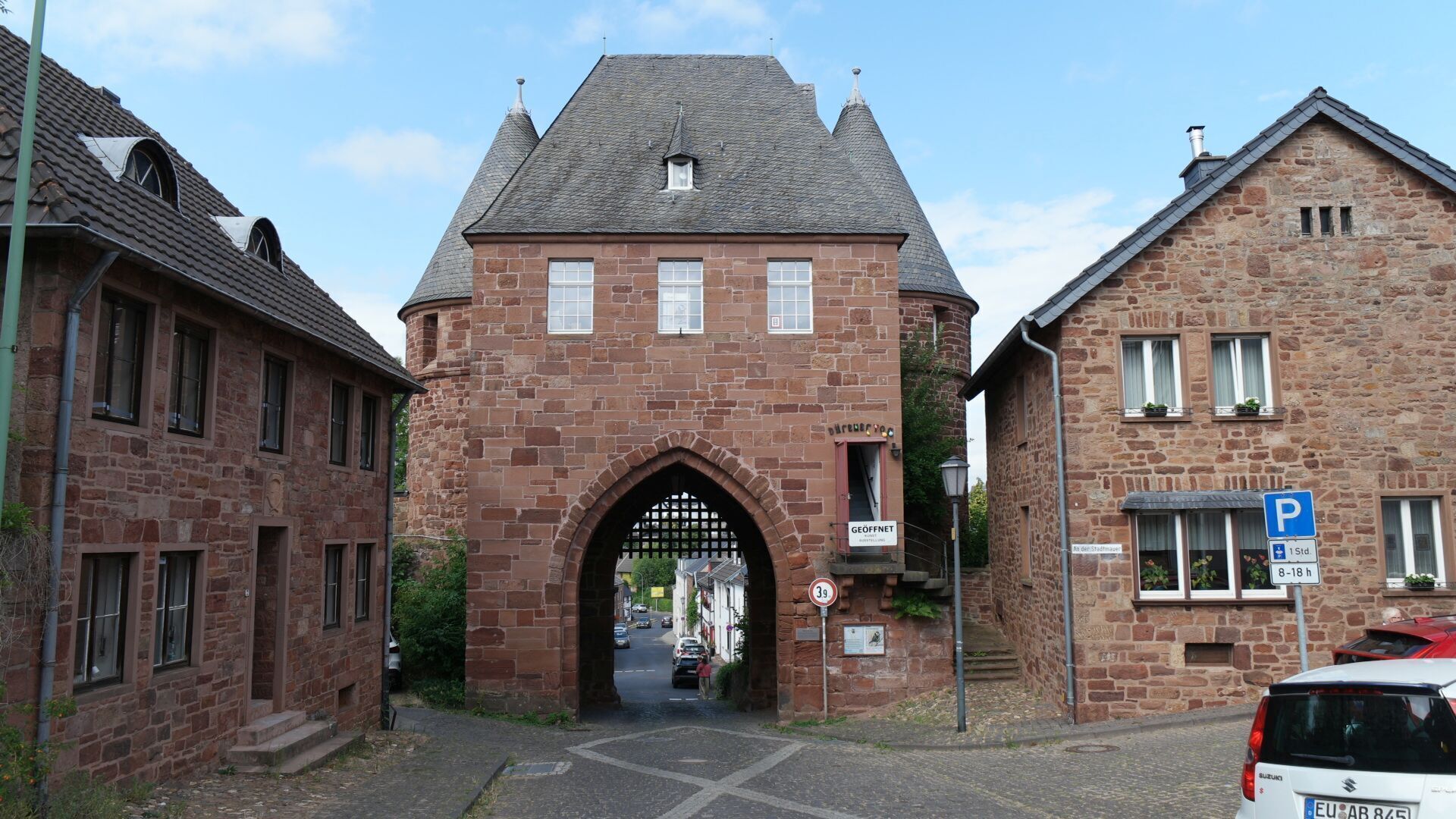 Ein Gebäude aus Stein mit einem zentralen Bogen, einem Parkschild und einem Fahrzeug.