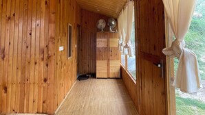 A wooden interior hallway with a door leading to a room, a window with curtains, and a pair of shoes on a mat.