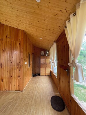 A wooden interior hallway with a door leading to a room, a window with curtains, and a pair of shoes on a mat. - Tranquil 1-bedroom cabin in marvelous Kullu for a cozy stay (kullu)